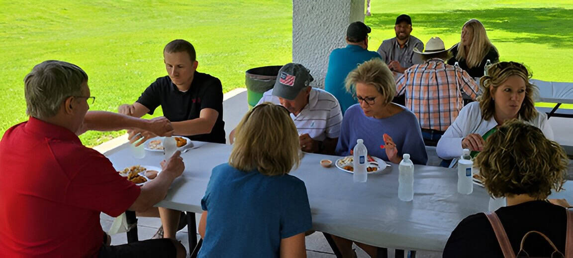Group of people enjoying an outdoor meal at a picnic table.