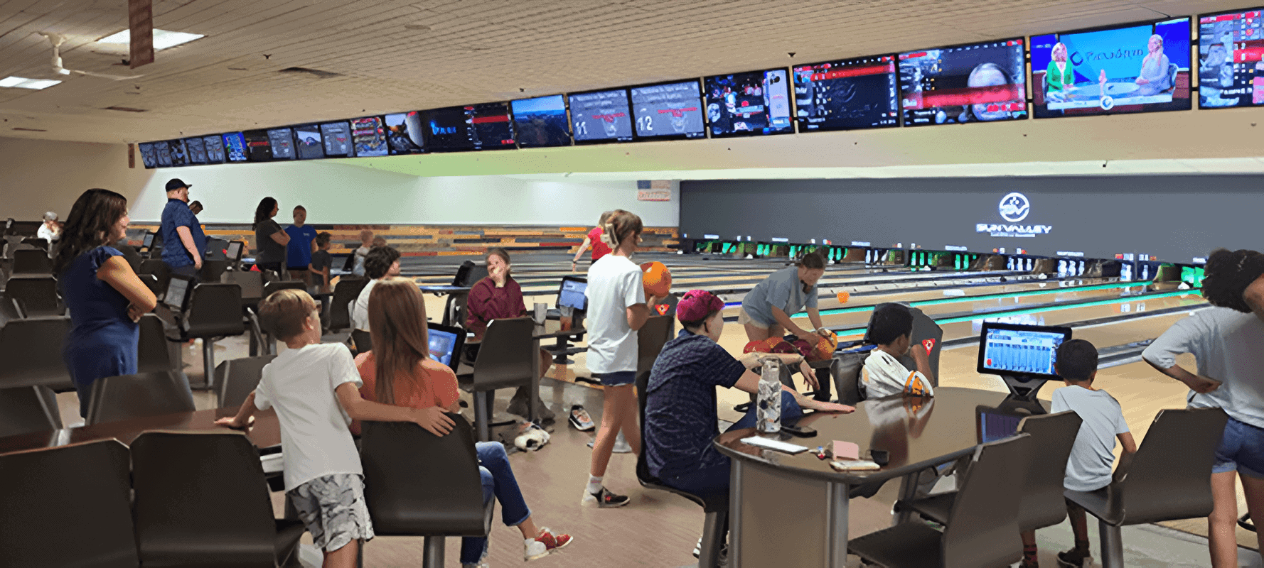 People enjoying bowling at a lively alley with multiple screens overhead.
