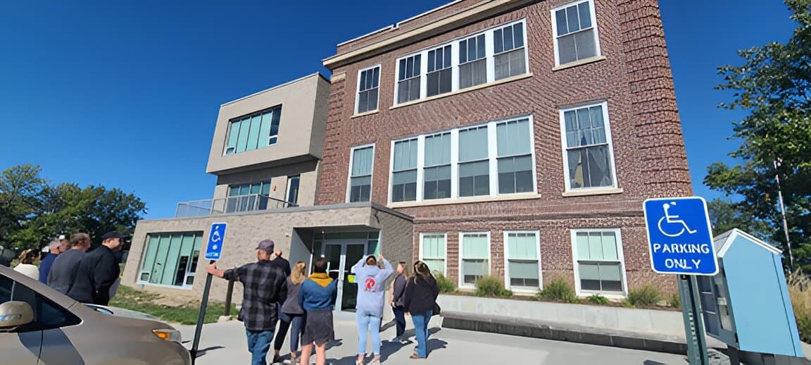 People gather outside a modern apartment building with accessible parking.