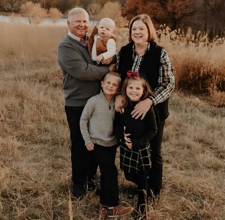Family photo of four with two children outdoors in a field during fall.