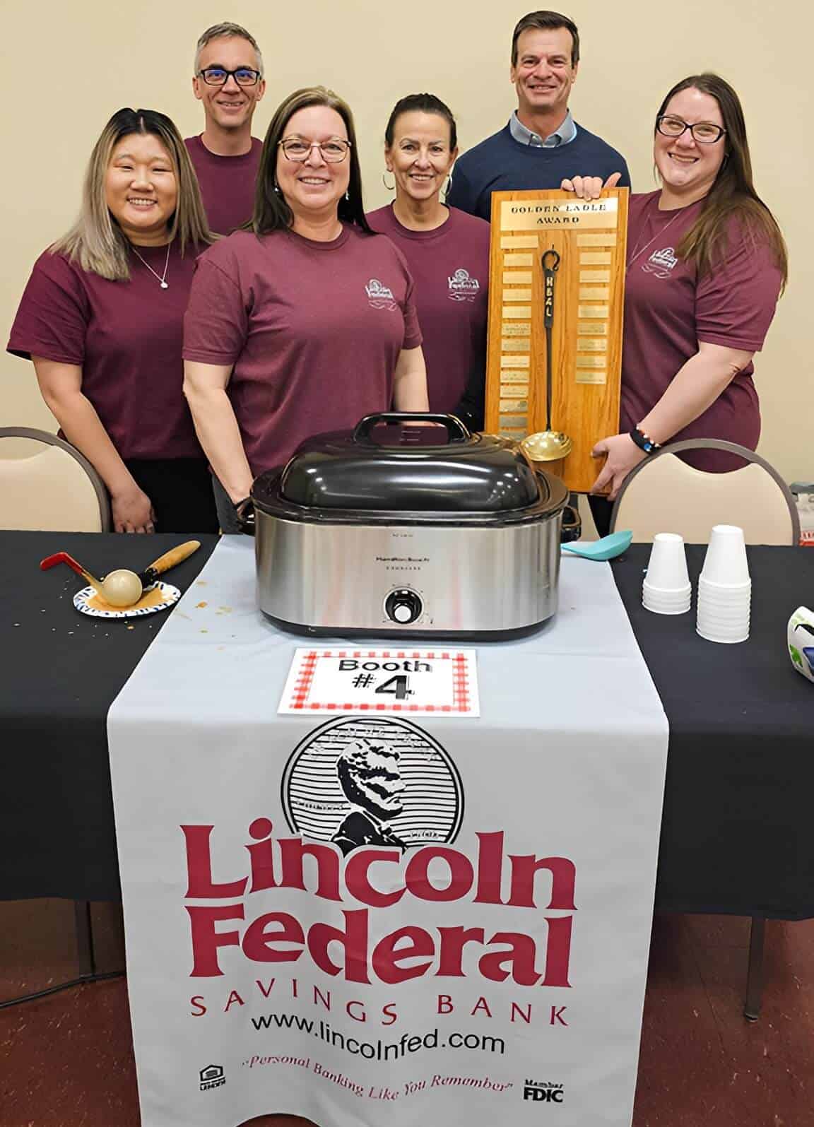 Group of six people at the 2024 Soup 'r Chili Contest, smiling behind a table with a Lincoln Federal.