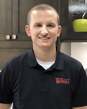 Young man in black polo shirt with Willet logo smiling in kitchen setting.