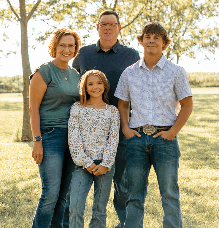 Family of four outdoors in a park with trees and sunlight.