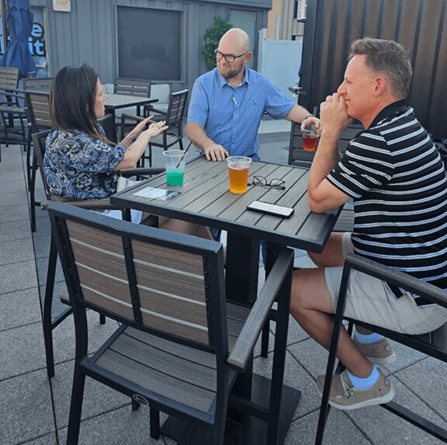 Three friends enjoying drinks and conversation on an outdoor patio.