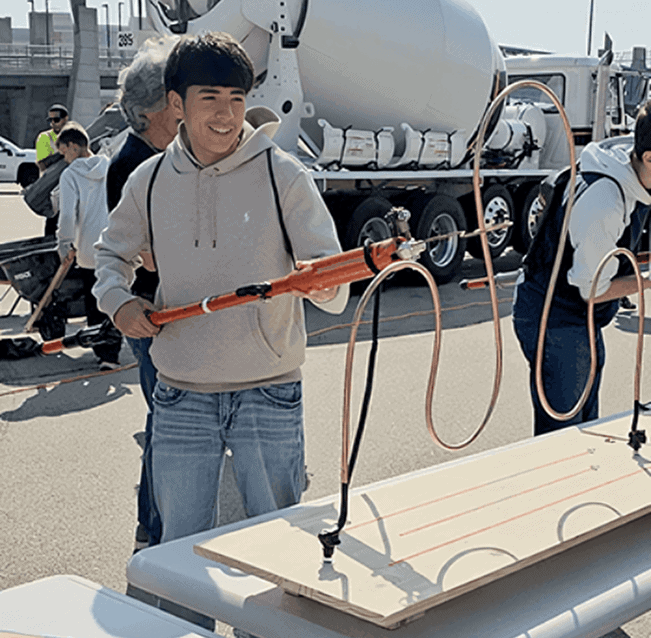 Young boy at construction career event holding a tool, smiling.