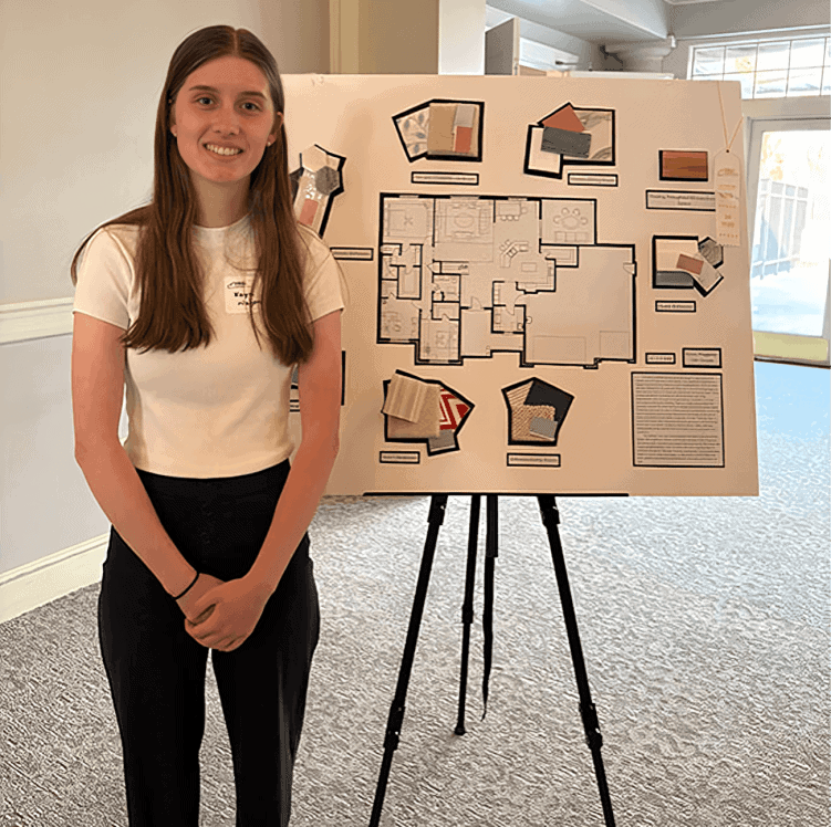Student presenting architectural design board with floor plan and samples.