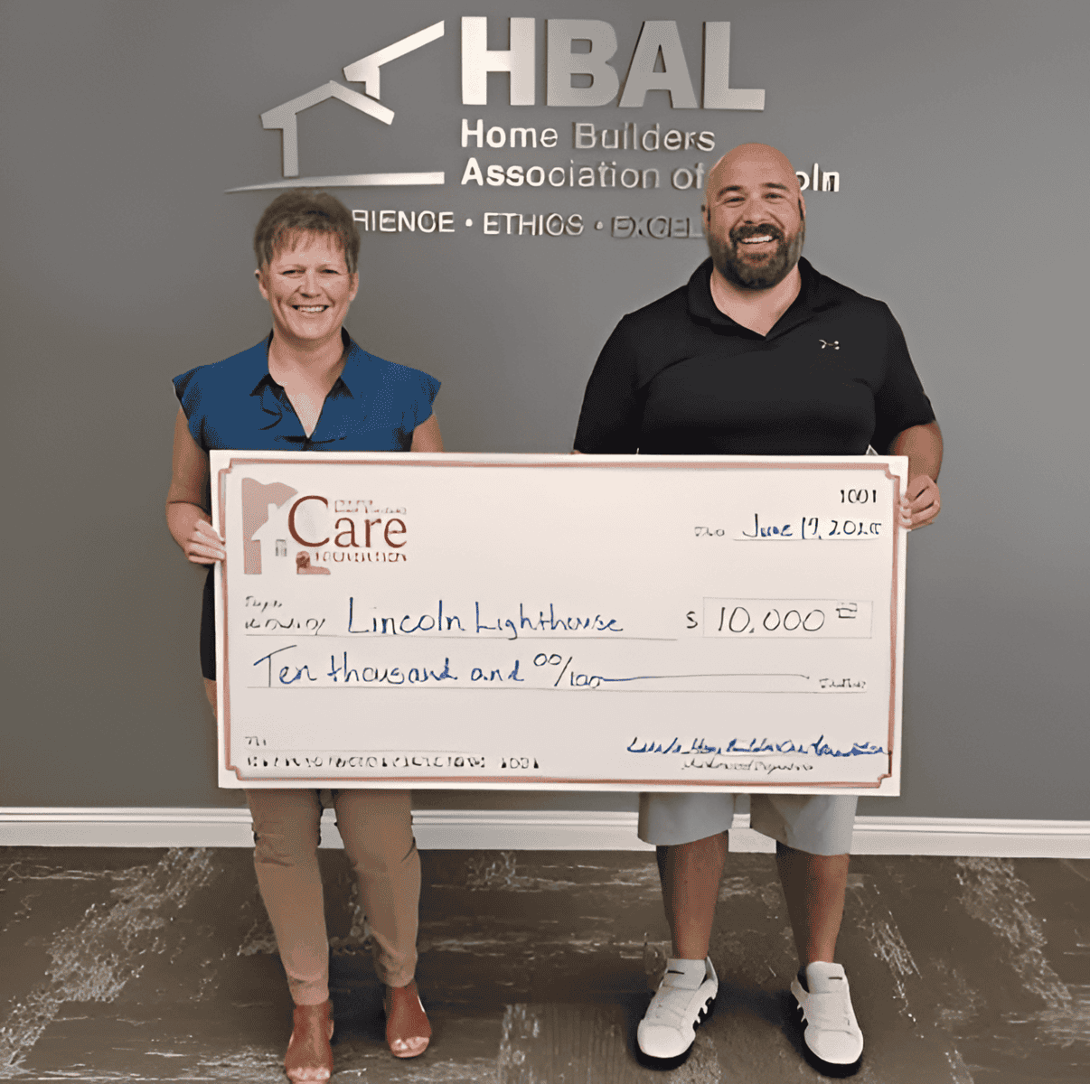 Two people holding a large check in front of a wall with HBAL logo.