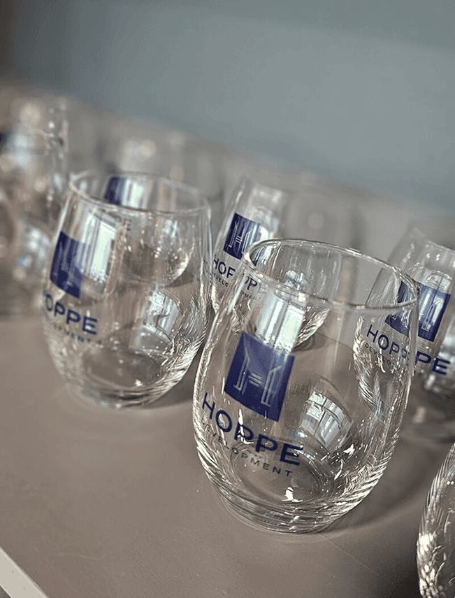 Clear glass cups with Hoppe Development logo on a table.