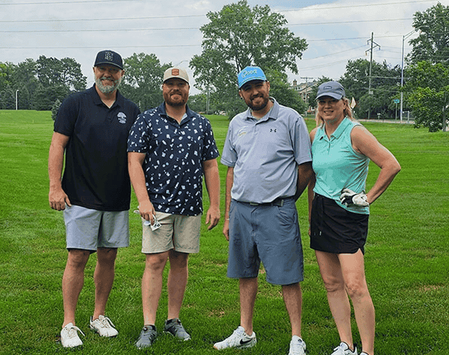 Four smiling people standing on a golf course, ready to play.